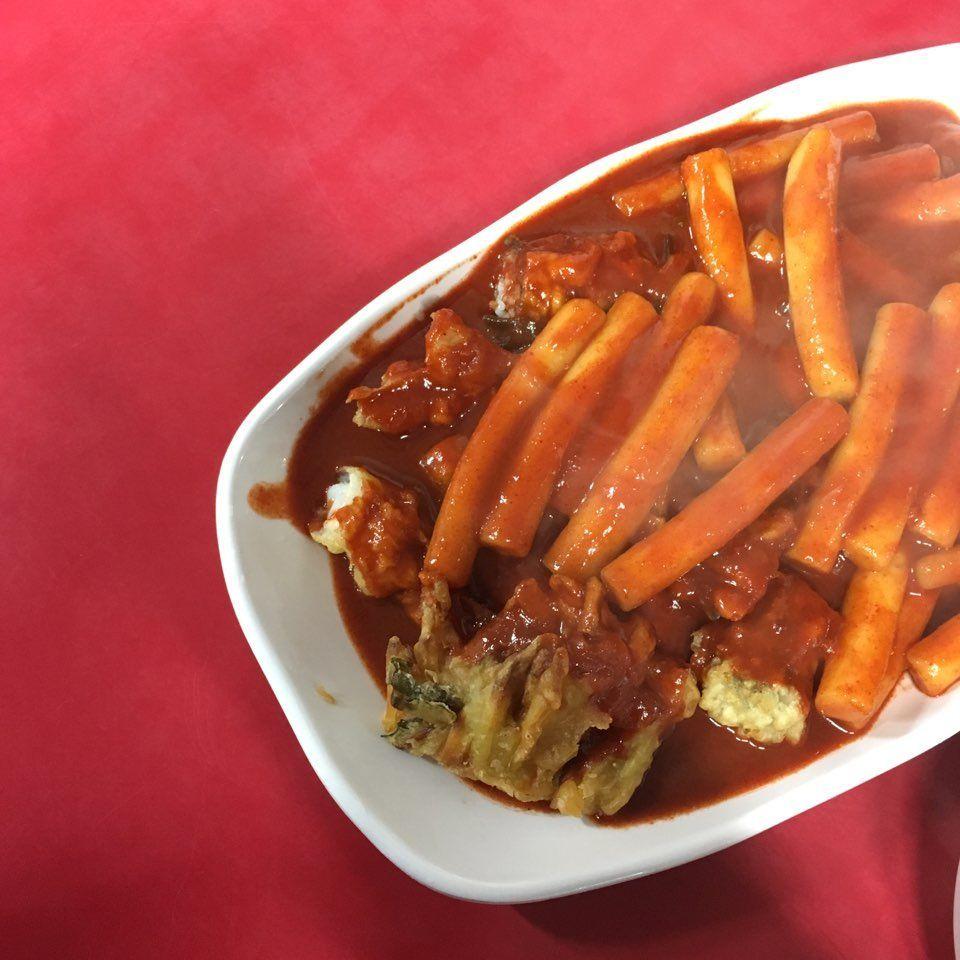 懸掛於布帳馬車前的一盤熟悉的辣炒年糕，讓人想起韓國街頭美食的濃鬱風味，展示小攤販的實景。